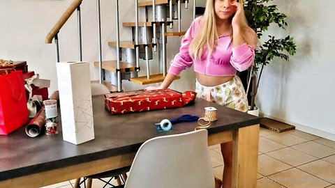 Young blonde in pink crop top and shorts wrapping sexy Christmas gifts teasing curves