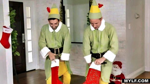 Two sexy elves in green Christmas costumes holding giant red stockings teasing for naughty holiday fun