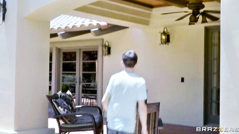 Clothed man in white t-shirt walking away on sunny patio towards chairs in Brazzers scene