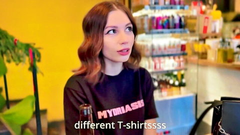 Red-haired woman in black Myrias t-shirt, casual store pose