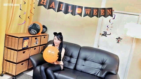 Busty Asian Halloween cat cosplay girl with huge tits holding pumpkin balloon on couch