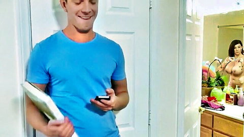 Smiling guy in blue shirt peeks at nude curvy brunette MILF's huge tits in bathroom mirror reflection