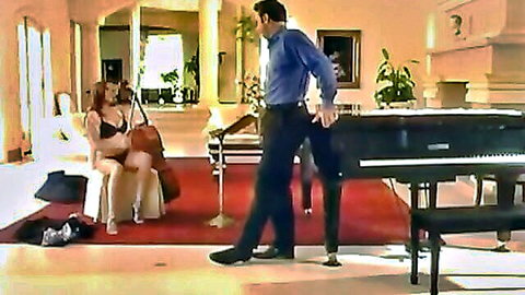 Busty redhead in black lace bra and thong sits seductively with cello as handsome man in shirt stands by grand piano
