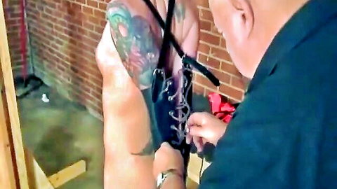 Clothed older man adjusts nipple chains on tattooed naked woman's exposed tits in CMNF BDSM play