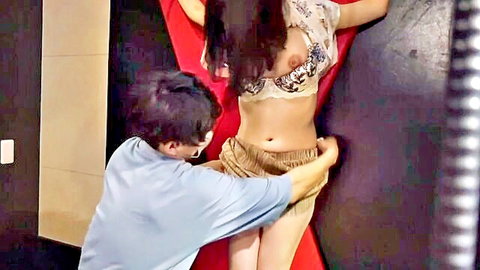 Skinny Japanese girl in see-through lace bra with exposed tits gets shorts pulled down by man against red BDSM wall