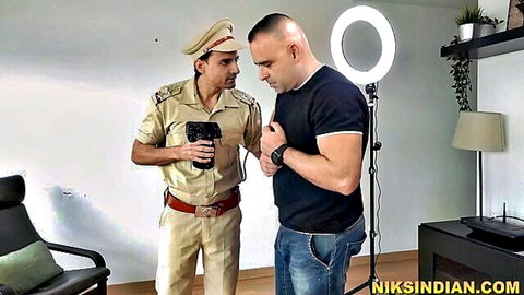 Indian police officer in uniform points gun at muscular bald man in black t-shirt and jeans