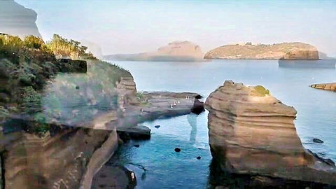 Serene coastal landscape with rocky cliffs, turquoise sea, and misty islands