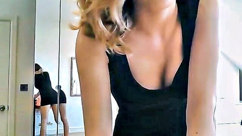 Blonde cam girl teasing in low-cut black dress, deep cleavage and curves