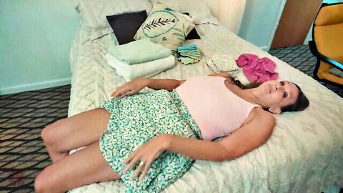 Mature MILF lying seductively on bed in pink top and floral skirt exposing thighs
