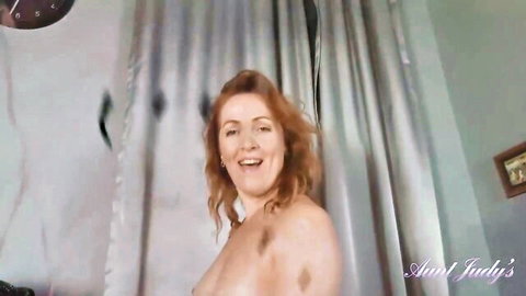 Smiling redhead MILF Aunt Judy exposes hairy natural tits topless