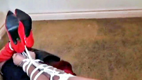 Woman's legs in red high heels and stockings tightly bound with white ropes in bondage play