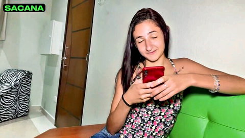 Young Latina amateur model smiling at red phone in floral tank top on casting couch