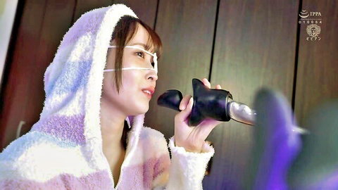 Masked Japanese babe in pink fluffy robe holds black dildo spoon toy to her lips teasingly