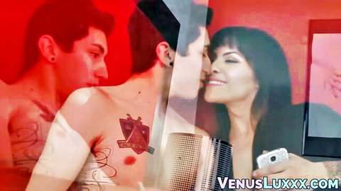 Tattooed shirtless hunk passionately kissing smiling brunette beauty in steamy red-lit double exposure
