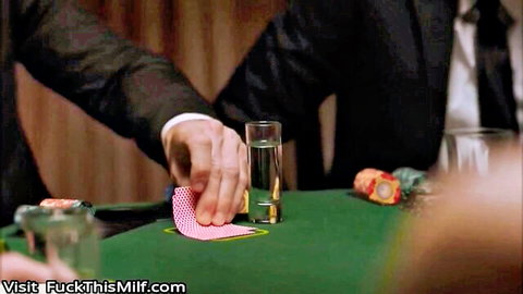 Man's suited hand holds pink poker chip over tequila shot glass on green felt table