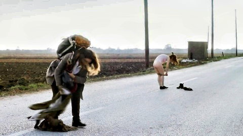 Brunette woman in tight pink leotard bends over outdoors on road near dog and friend