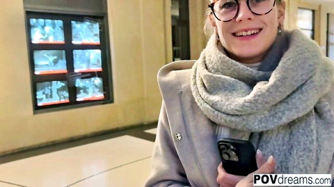 Smiling German blonde tourist in gray coat and scarf holding phone, POV pickup in Prague