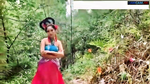 Exotic Asian woman in blue top and red skirt posing in lush jungle for Erotic Ghost Story 2020