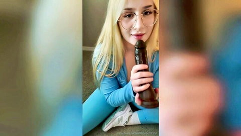 Blonde with glasses in tight blue outfit teases blowjob on huge black dildo smiling seductively