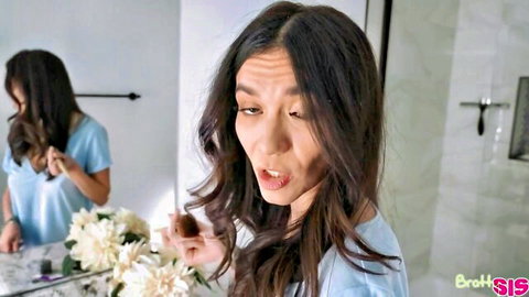 Naughty brunette teen in blue top makes surprised face holding brush in bathroom mirror selfie
