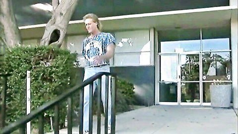 Vintage blonde hunk in Hawaiian shirt stands outside building before threesome action
