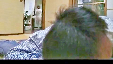 Japanese woman in white dress approaches older man on futon in JAV scene