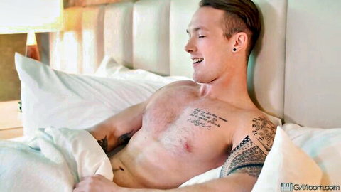 Tattooed muscular man smiling shirtless in bed, in-house masseur trans sex scene
