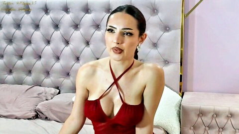 Brunette babe in tight red halter dress with deep cleavage pouting seductively on bed