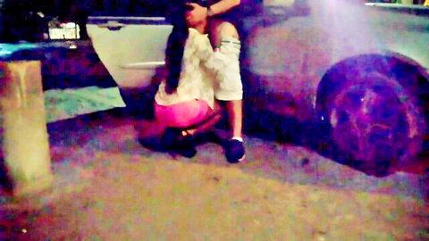 Curvy woman teasing in pink shorts and white top by car at night