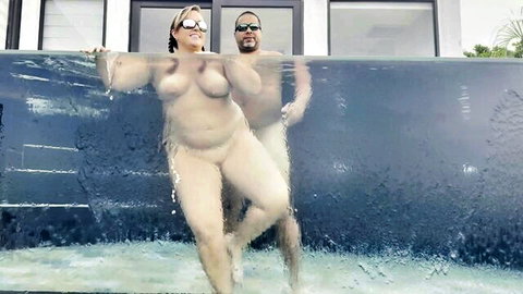 Nude BBW MILF and black stud embracing in outdoor pool