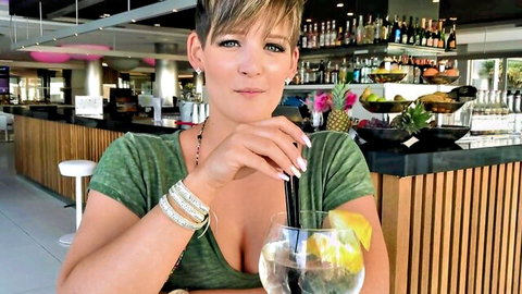 Blonde with big tits in low-cut top sips cocktail teasing deep cleavage at bar