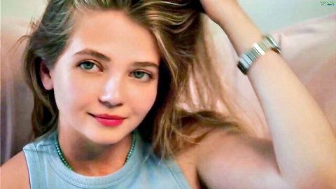 Young webcam girl with green eyes smiling seductively in tight blue tank top showing cleavage
