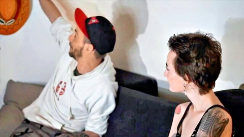 Katya with short hair and tattoo interviews man in cap