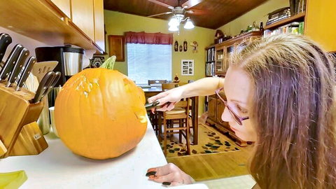 Mature redhead with glasses carving pumpkin in kitchen