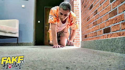 Short-haired man in orange floral shirt kneeling on floor in brick hallway