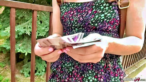 Petite babe in floral dress holding thick wad of cash outdoors by railing