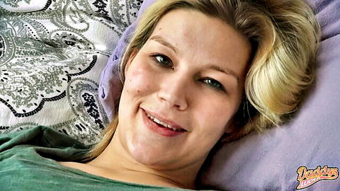 Smiling blonde MILF teases with medium tits cleavage on bed