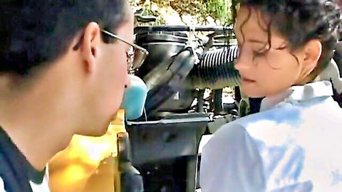 Curly-haired teen girl gazes intimately at guy inches from kissing near car engine