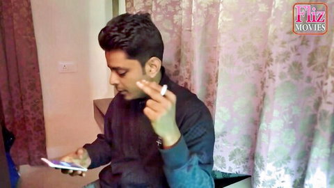 Indian guy in dark jacket smokes cigarette while checking phone in hotel room