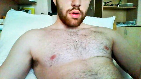 Hairy bearded man puckers lips blowing kiss shirtless exposing chest hair on bed