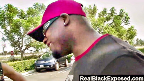 Black man in pink D&G hat and sunglasses smiles outdoors near blue SUV