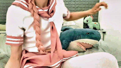 Femboy in sailor uniform relaxing on bed with plush toys after work