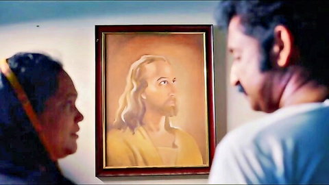 South Asian couple gazing at Jesus Christ portrait on wall in dim room
