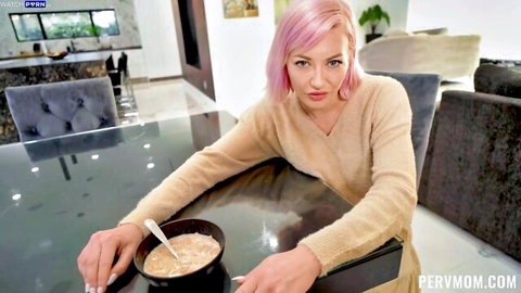 Pink-haired MILF in beige sweater holds spoon over cereal bowl at kitchen table POV