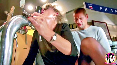 Mature blonde granny in stockings teases phallic beer tap at bar with man watching