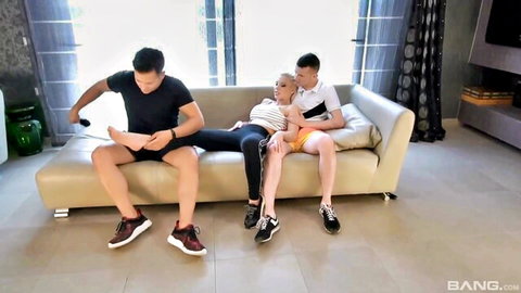 Curvy blonde with huge tits sprawled across two Asian guys' laps while gaming on couch