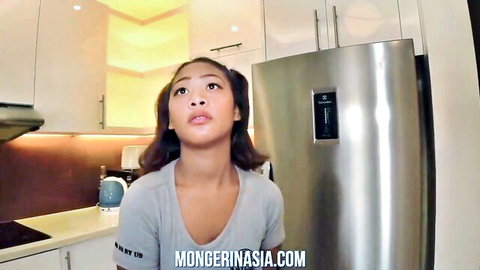 Cute Asian brunette in low-cut gray top showing cleavage looking up with open mouth in kitchen