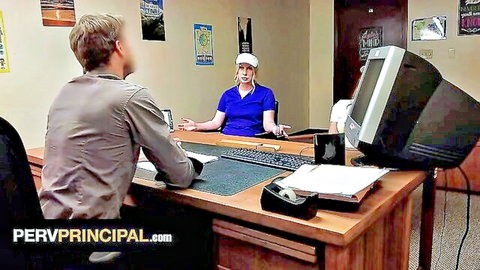 Blonde woman in blue polo and visor cap gestures at principal's desk in office