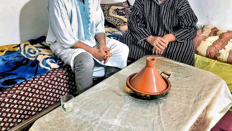 Two Moroccan men in traditional djellabas seated intimately with tajine