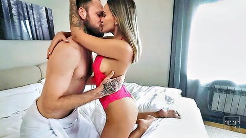 Tattooed muscular guy in towel passionately kisses busty blonde in skimpy pink lace lingerie on bed
